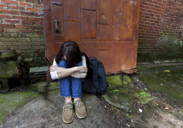 Young teenager down and out in an alley on the street too afraid to allow someone to help her