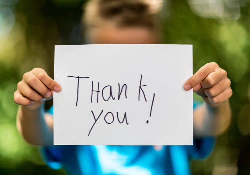 Blurred boy holding a piece of paper with the words Thank You in front of her.