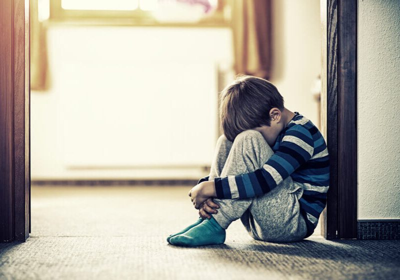 Depressed sad child sitting on the floor, in the door. The little boy is hiding his head between legs.