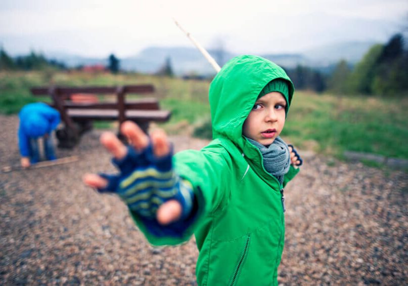 Little boys playing jedi knights using sticks and imagination. The boy aged 4 is using his special powers and holding his wooden 'lightsaber'. The boy in the background is picking up his weapon from the ground.