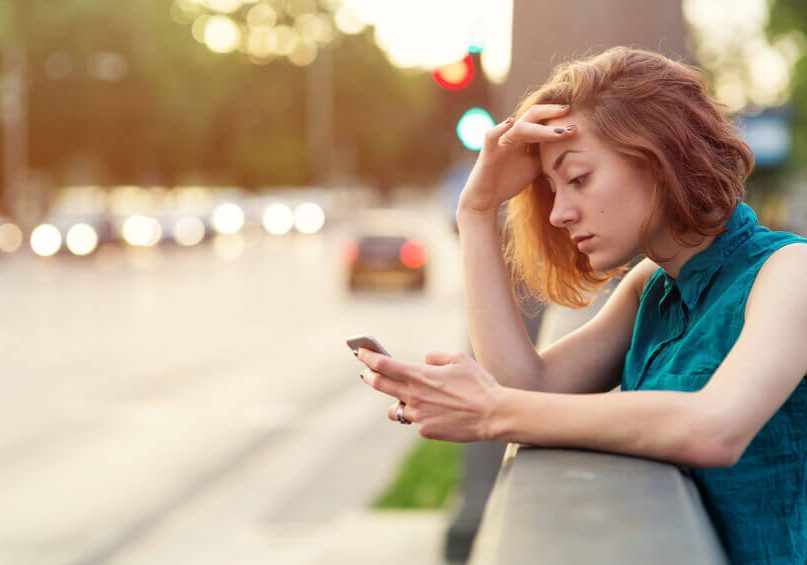 Teenage girl staying on a sidewalk near the boulevard and staring at her cell phone.
