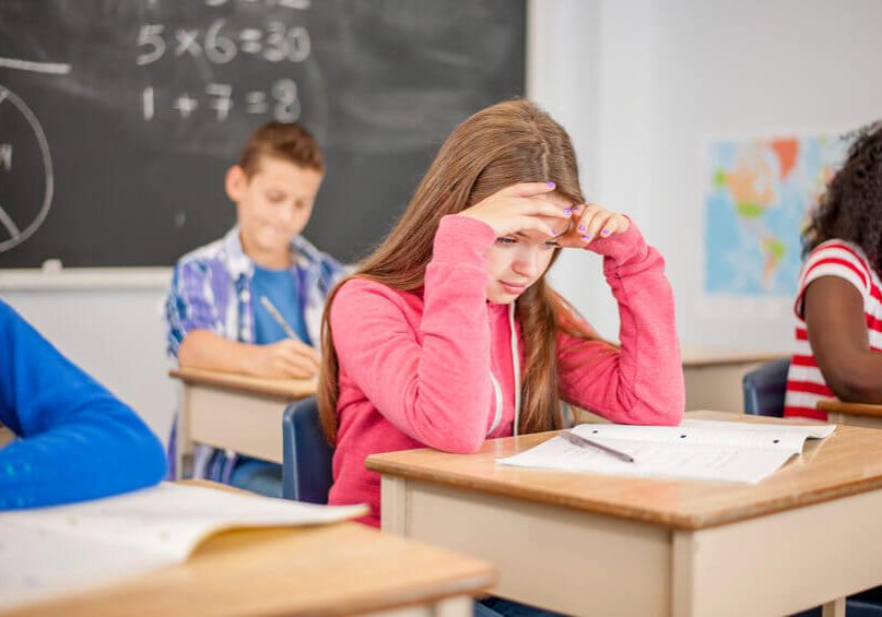 A multi-ethnic group of elementary age students are taking a test in class. One girl is stressed about the questions on the test.