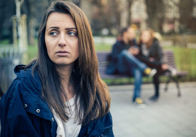 Lonely single girl feeling depressed because of a happy couple laughing on the next bench.